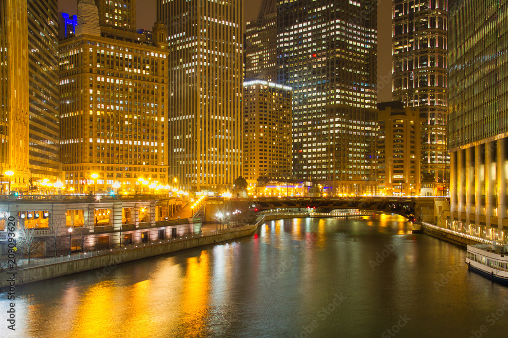 Yellow lights reflecting on the buildings and water of the Chicago River at night.