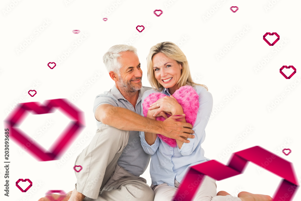 Happy couple sitting and holding heart pillow against hearts Happy couple sitting and holding heart pillow against hearts