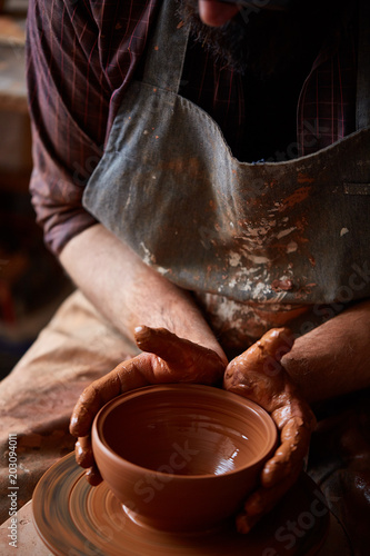 Close-up hands of a male potter in apron molds bowl from clay, selective focus photo