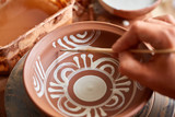 A potter paints a clay plate in a white in the workshop, top view, close-up, selective focus.