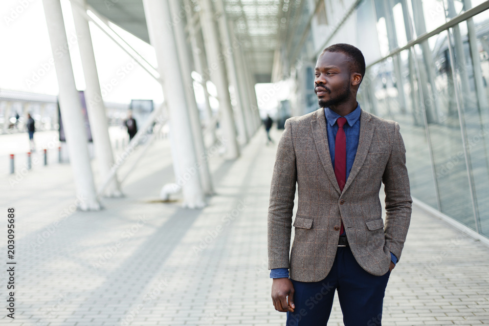 Stylish African American black businessman poses in a suit before a modern glass building outside Stylish African American black businessman poses in a suit before a modern glass building outside