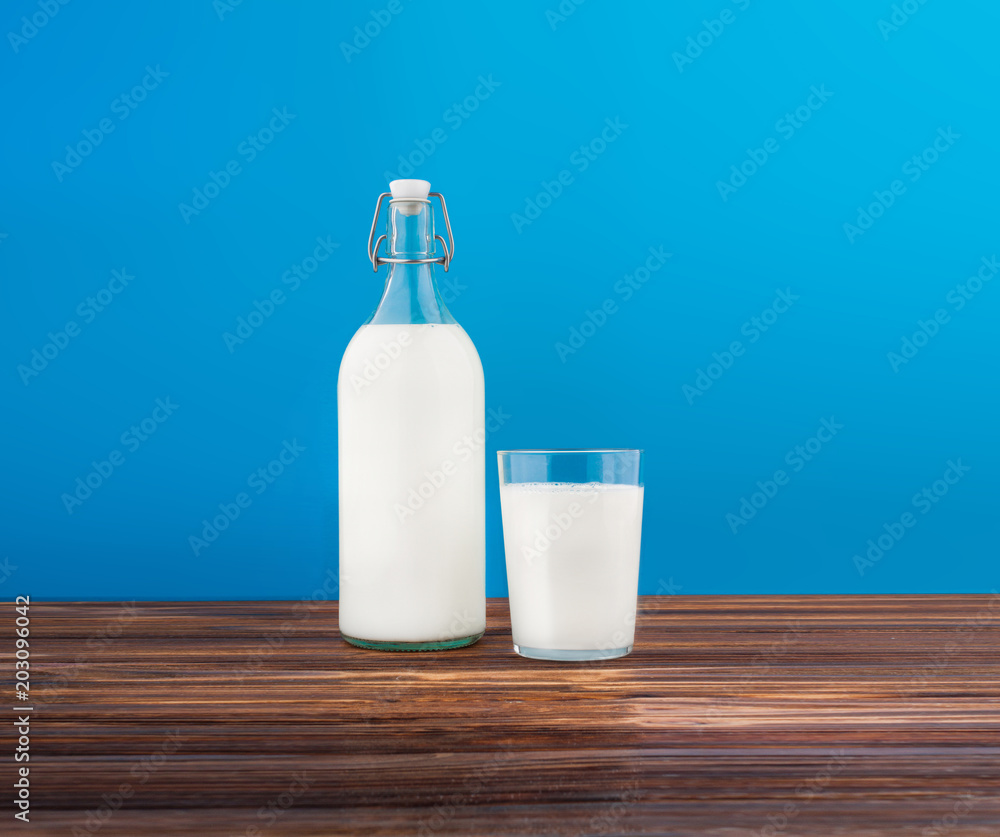 a glass of milk, a bottle of milk on a wooden table on a colored background a glass of milk, a bottle of milk on a wooden table on a colored background