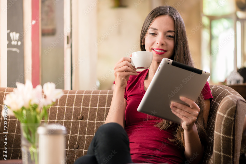 Contemporary young woman smiling while reading on tablet in a coffee shop Contemporary young woman smiling while reading on tablet in a coffee shop