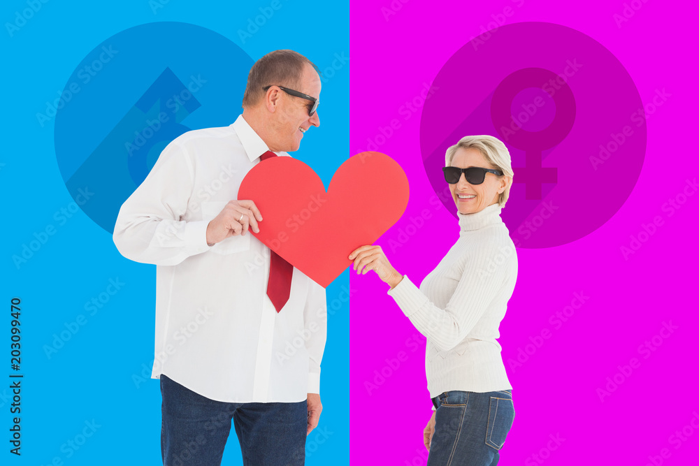 Older affectionate couple holding red heart shape against pink and blue Older affectionate couple holding red heart shape against pink and blue
