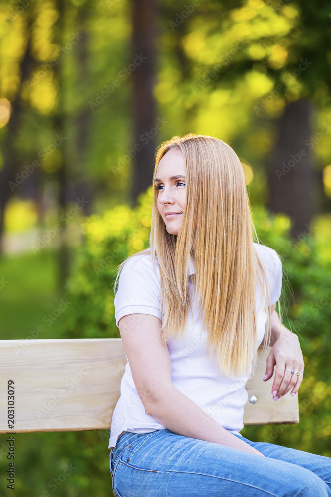 Young, happy, thin young blond woman with long beautiful hair, smiling, in the summer park under the rays of the sun Young, happy, thin young blond woman with long beautiful hair, smiling, in the summer park under the rays of the sun