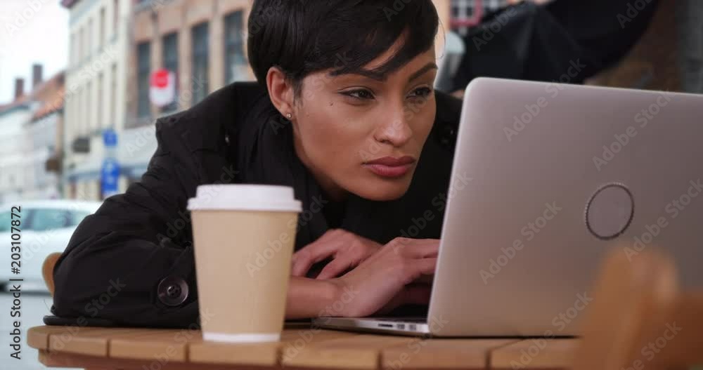 African millennial female using her laptop computer outdoors at a local cafe, Black young lady reads her emails on her laptop while in a European setting, 4k African millennial female using her laptop computer outdoors at a local cafe, Black young lady reads her emails on her laptop while in a European setting, 4k