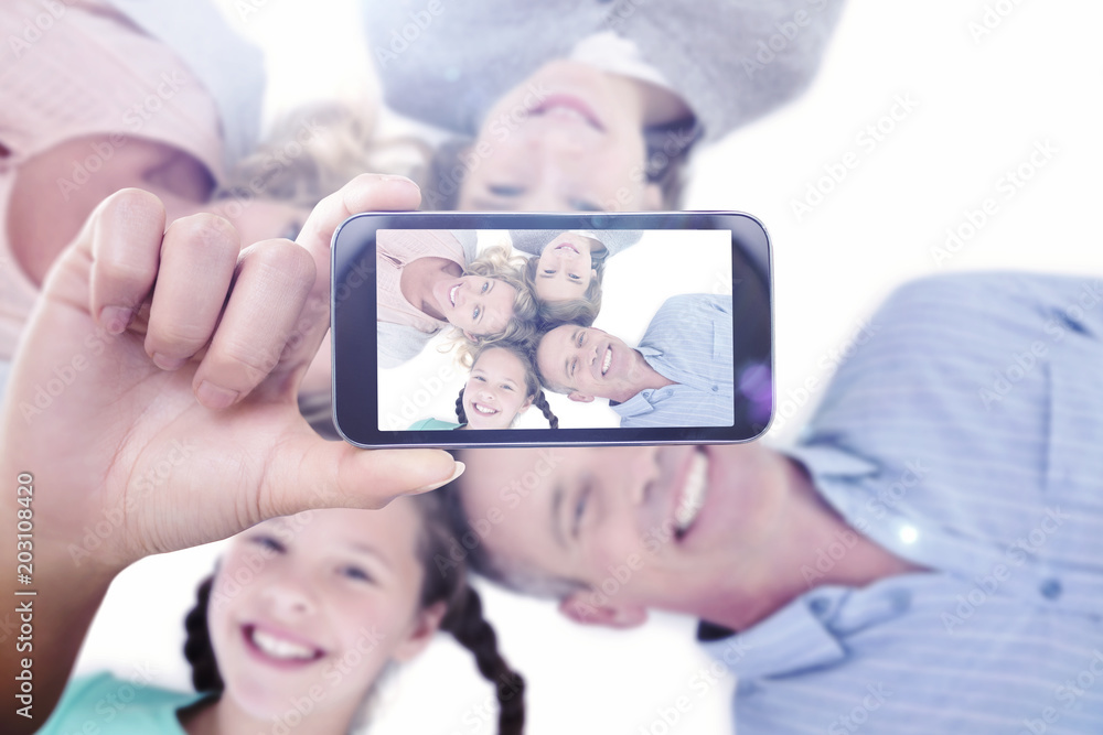 Hand holding smartphone showing against overhead of smiling family lying together in a circle