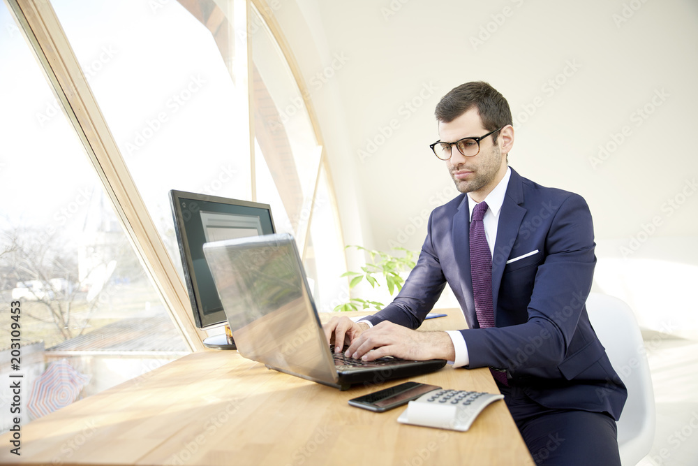 Businessman using laptop. Portrait of young financial assistant businessman wearing suit while sitting at office desk and working on financial report. Businessman using laptop. Portrait of young financial assistant businessman wearing suit while sitting at office desk and working on financial report.