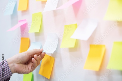 close up hand people business man post it notes in the wall at meeting room. Sticky note paper reminder schedule board. Colorful variety copy empty space. soft focus.