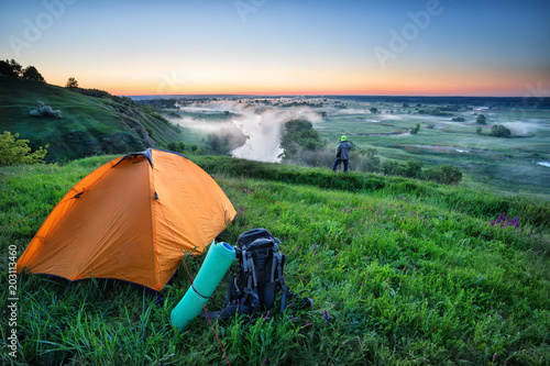 Orange tent and backpack on hill with tourist