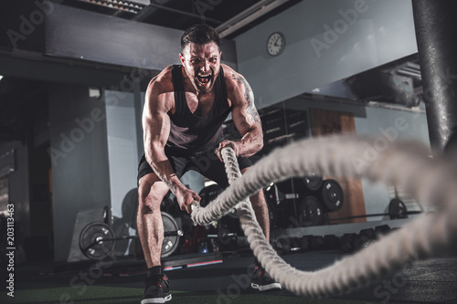 Muscular powerful aggressive man working out with rope in functional training fitness gym photo