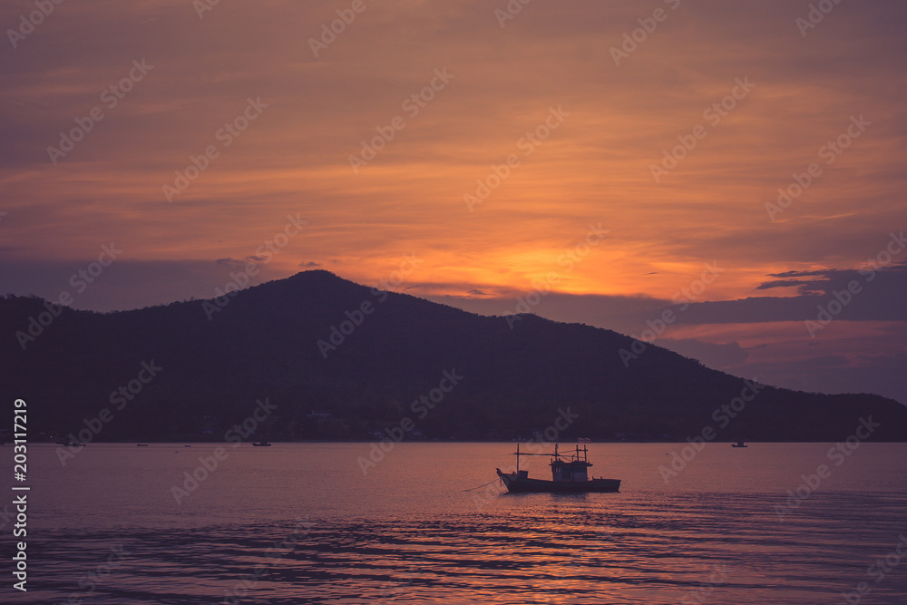 Beautiful seascape view of fishing boat floating on the sea with sunset light in the background at twilight time. (Selective focus)