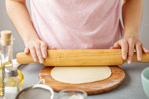 Woman roll out the dough on the wooden cutting board.