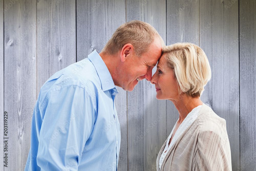 Happy mature couple facing each other against wooden planks Happy mature couple facing each other against wooden planks