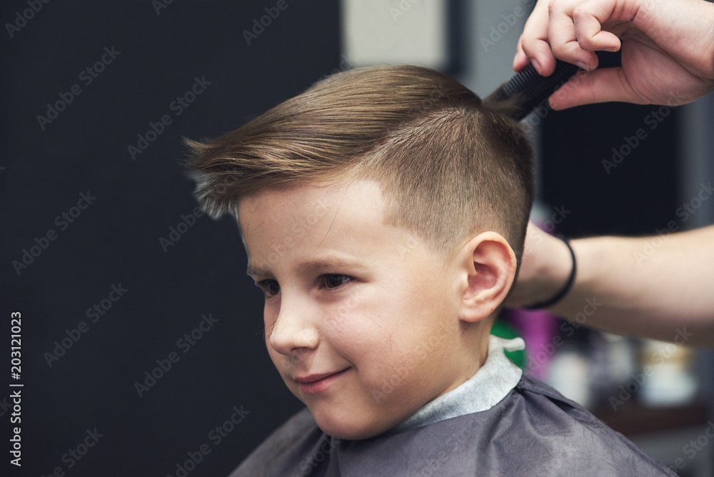 European boy getting hairstyle in barbershop.