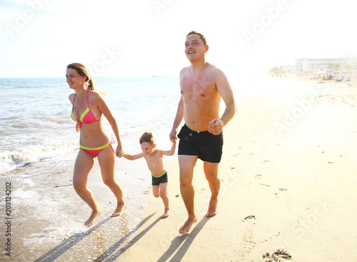 Happy young family having fun running on beach at sunset. Family traveling concept.