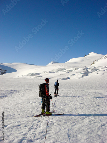 two male backcountry ski mountaineers head towards a high alpine peak over a long glacier between Saas Fee and Zermatt © makasana photo