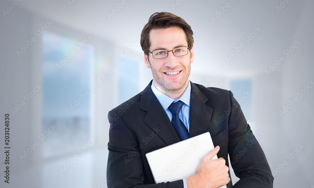 Smiling businessman holding his laptop looking at camera against bright white hall with columns Smiling businessman holding his laptop looking at camera against bright white hall with columns
