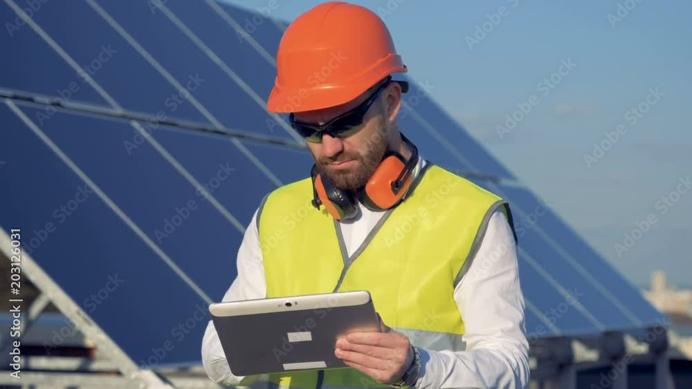 Engineer uses his tablet to work, standing next to solar panels on the roof. Engineer uses his tablet to work, standing next to solar panels on the roof.