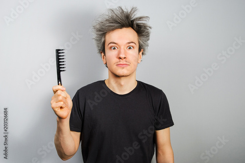 Unshorn and unshaven young guy holds comb on gray background. photo