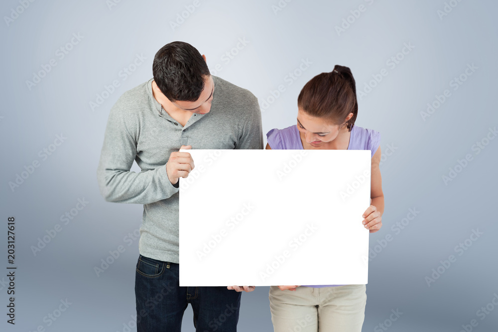 Young couple holding banner together and looking down against grey vignette Young couple holding banner together and looking down against grey vignette