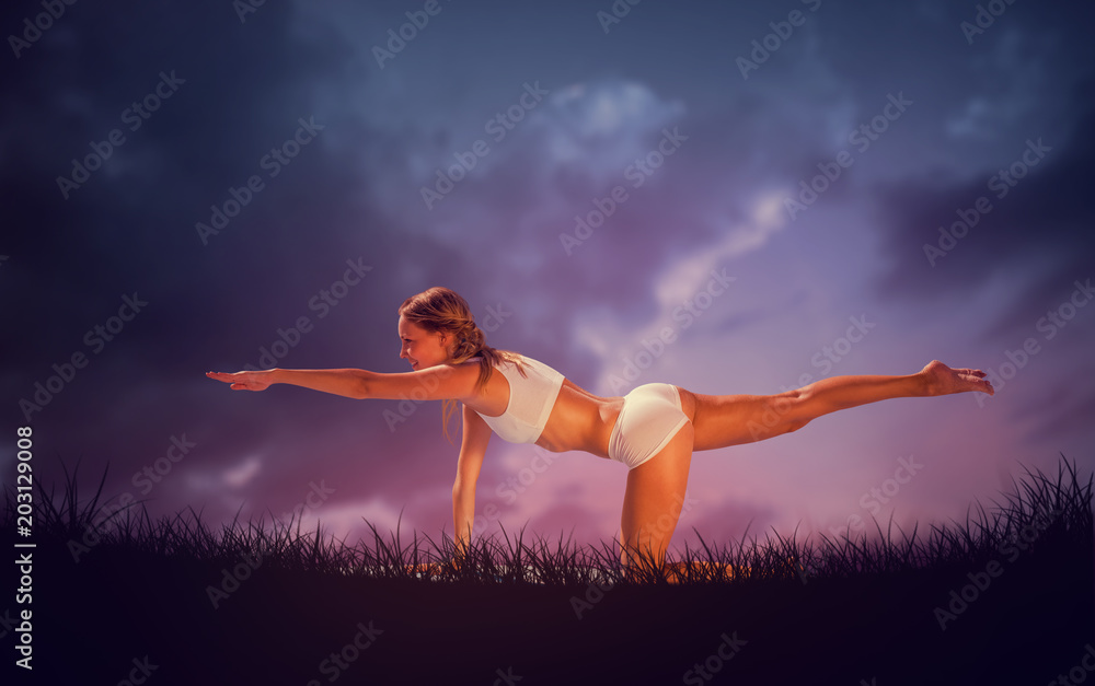 Gorgeous fit blonde in pilates pose on the beach against blue sky over grass