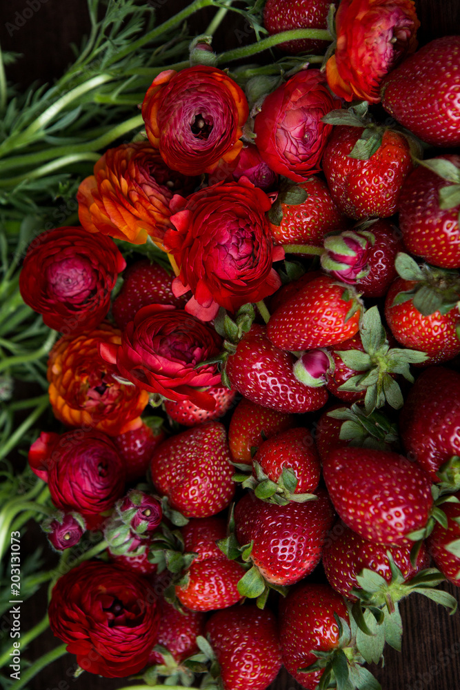 red fresh strawberry lies next to red flowers red fresh strawberry lies next to red flowers