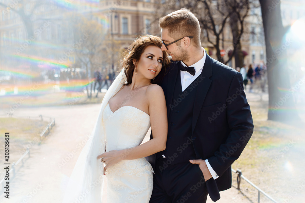 Fototapeta premium Newlywed couple bride and groom photoshoot after wedding ceremony in Saint-Petersburg Russia. White wedding dress with long veil and classical black suit or smoking with bowtie. Businessman in glasses