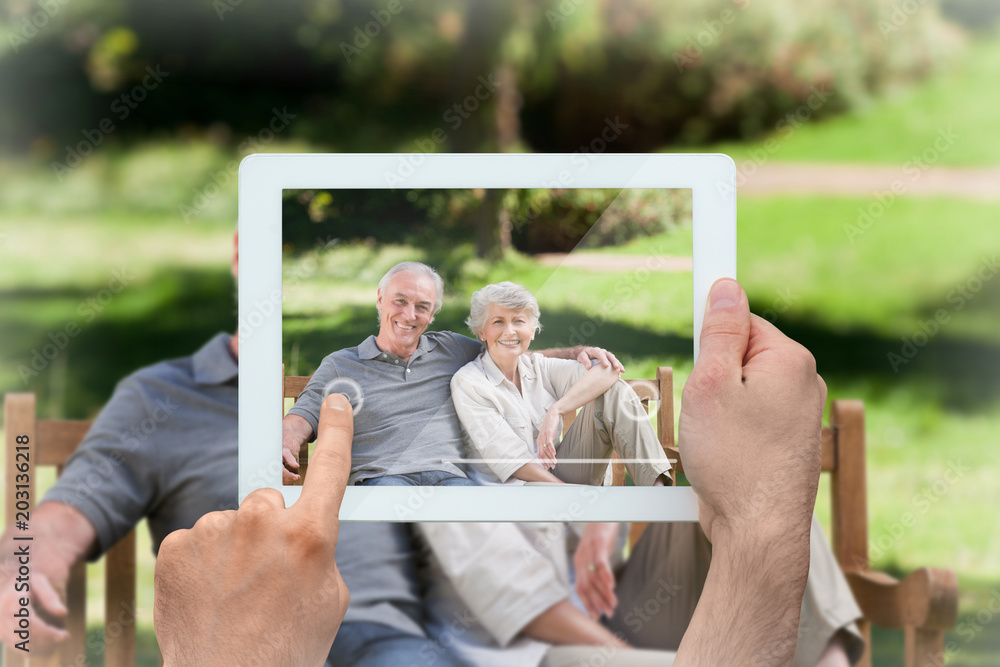 Hand holding tablet pc showing senior couple sitting on a bench