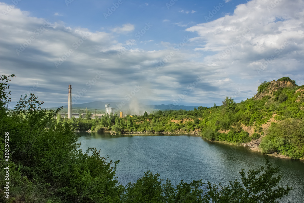 soft focus pollution concept with nature quarry landscape and lake on foreground and industrial factory on background
