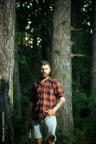 Brutal lumberjack in woods. Bearded guy holding small spade in his hands. Environment and nature concept