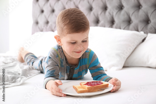 Cute little boy eating toast with sweet jam on bed