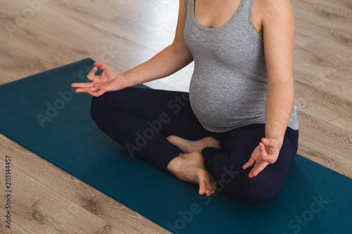 Young pregnant woman in a yoga studio meditating on a mat