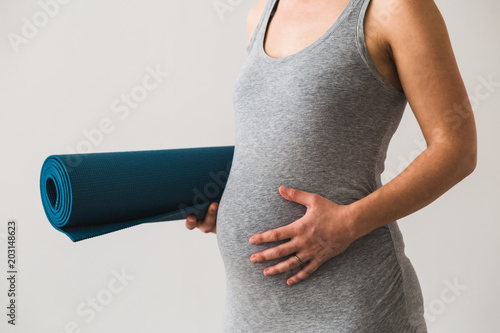 Young woman in early pregnancy with rolled mat under her arm going to prenatal yoga class photo