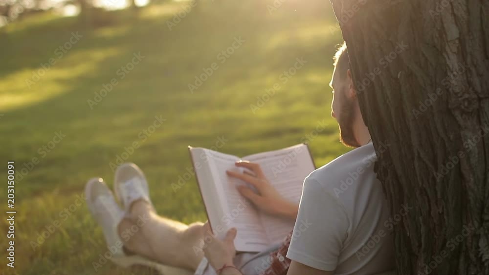 A young guy reading a book under a tree in the nature A young guy reading a book under a tree in the nature