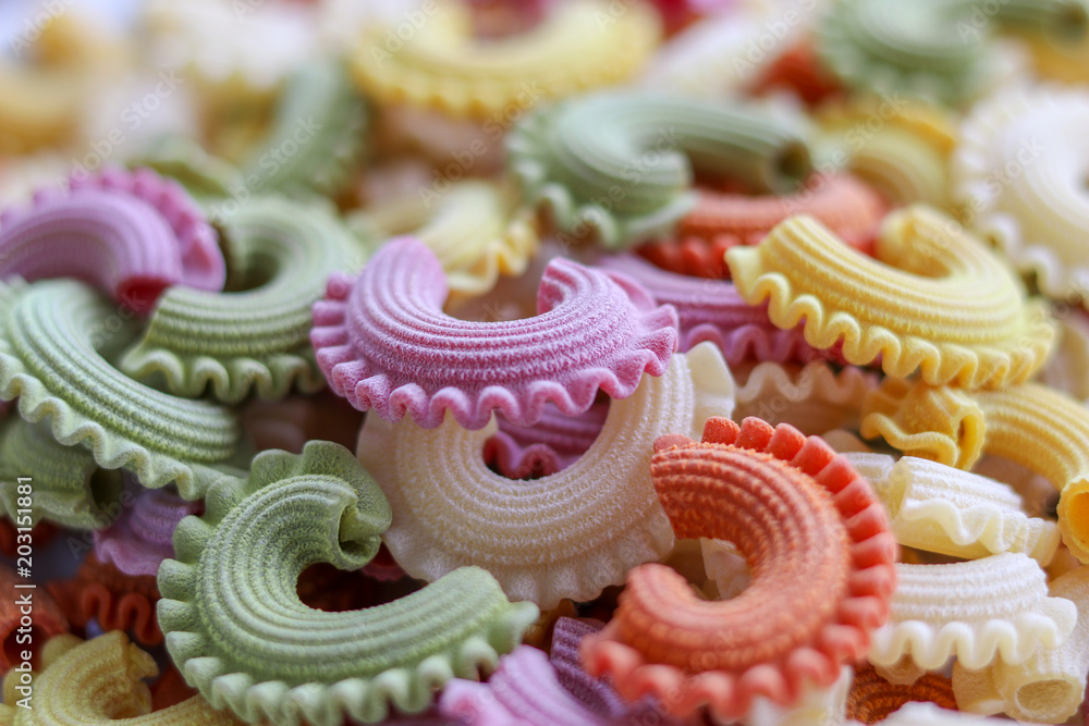 Background of colorful green, yellow, white, orange and pink italian crown pasta as creative food texture, close-up. Multicolor pasta texture pattern.  Front focus