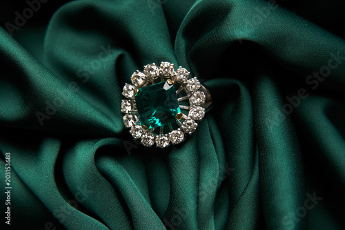 Green emerald fashion engagement diamond ring on green satin background. Luxury female jewellery, close-up. Selective focus