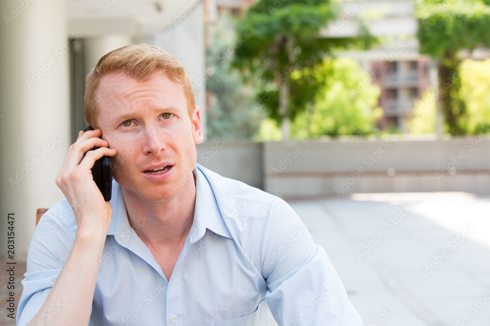 Closeup portrait, young man annoyed, frustrated, pissed off by someone talking on his mobile phone, bad news, isolated outdoors outside background. Long wait times, horrible conversations concept Closeup portrait, young man annoyed, frustrated, pissed off by someone talking on his mobile phone, bad news, isolated outdoors outside background. Long wait times, horrible conversations concept