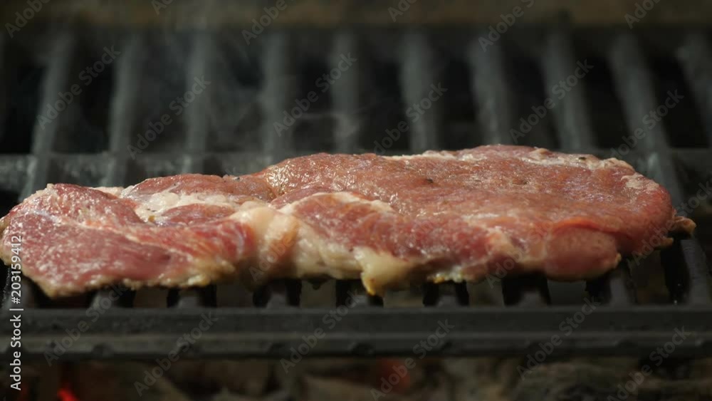 Semislotte steak lies on the grill, in the background smoke from the grill, view of the video with the side close-up, macro Semislotte steak lies on the grill, in the background smoke from the grill, view of the video with the side close-up, macro