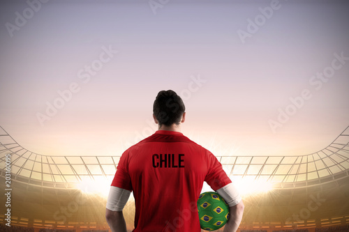 Chile football player holding ball against large football stadium under blue sky © vectorfusionart
