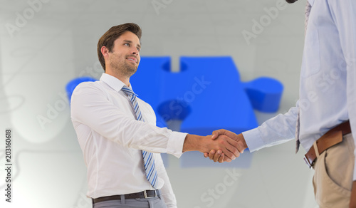 Young businessmen shaking hands in office against jigsaw 