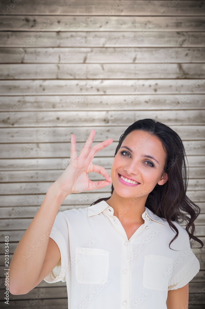 Pretty brunette making ok sign against wooden planks background Pretty brunette making ok sign against wooden planks background