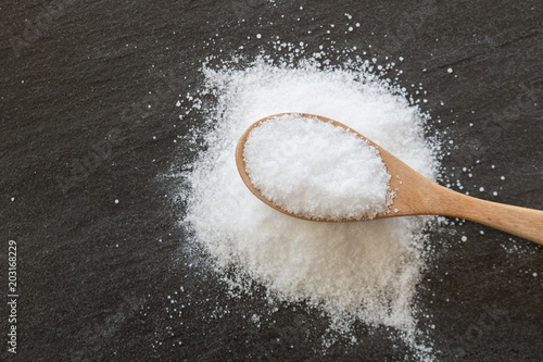 White salt in wooden spoon with black background.