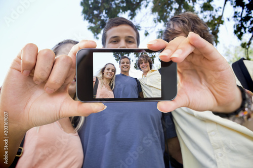 Hand holding smartphone showing low angleshot of three students shoulder to shoulder photo