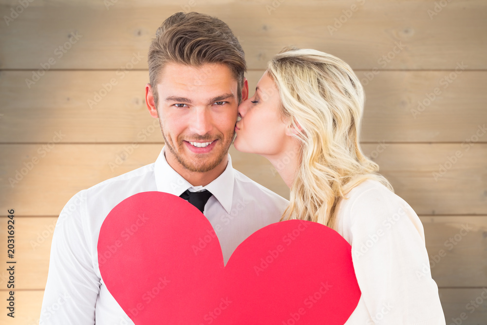 Attractive young couple holding red heart against bleached wooden planks background