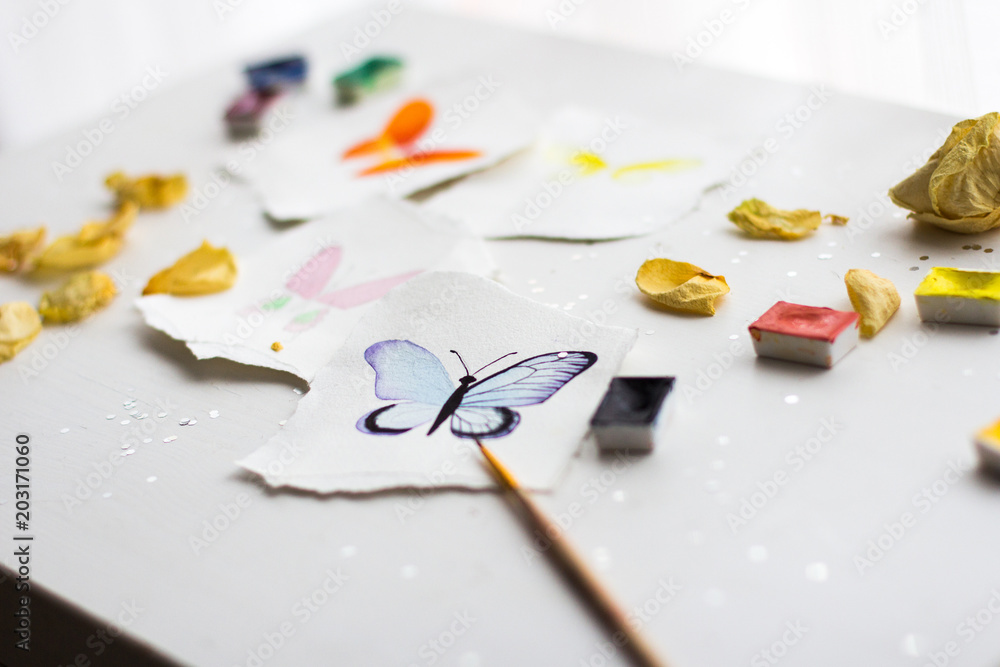 watercolor sketches of butterflies on the paper with torn edges on a white background with decorations, confetti, and dried flowers