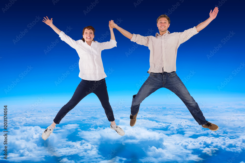 Couple jumping and holding hands against blue sky over clouds at high altitude