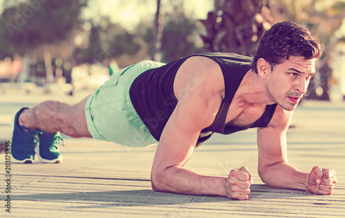 Strong sporty man doing press exercises holding plank outdoors © JackF