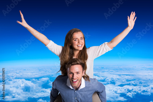 Smiling young man carrying woman against blue sky over clouds at high altitude