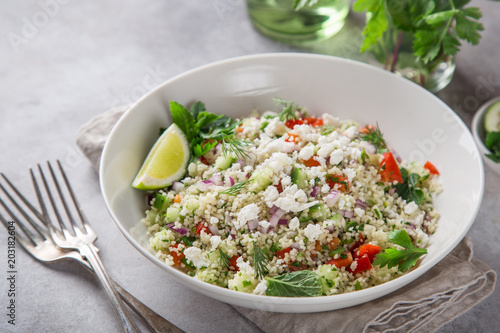 couscous and vegetables salad with feta cheese in white bowl